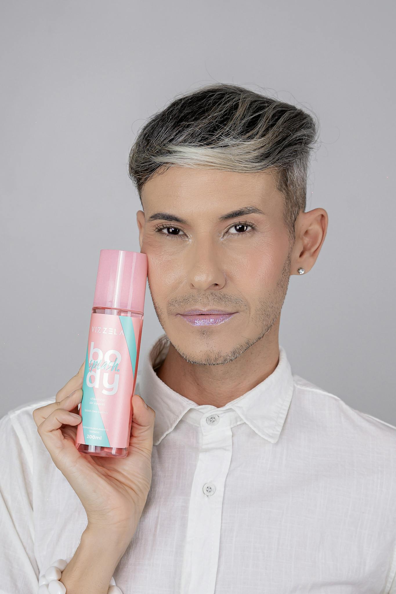 Man showcasing pink beauty product against neutral background.